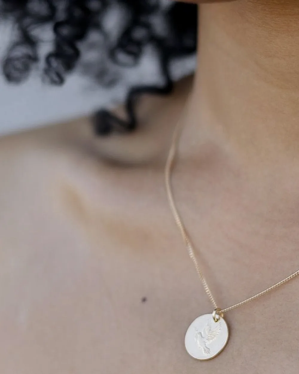 Round pendant necklace worn at the neckline for scale.