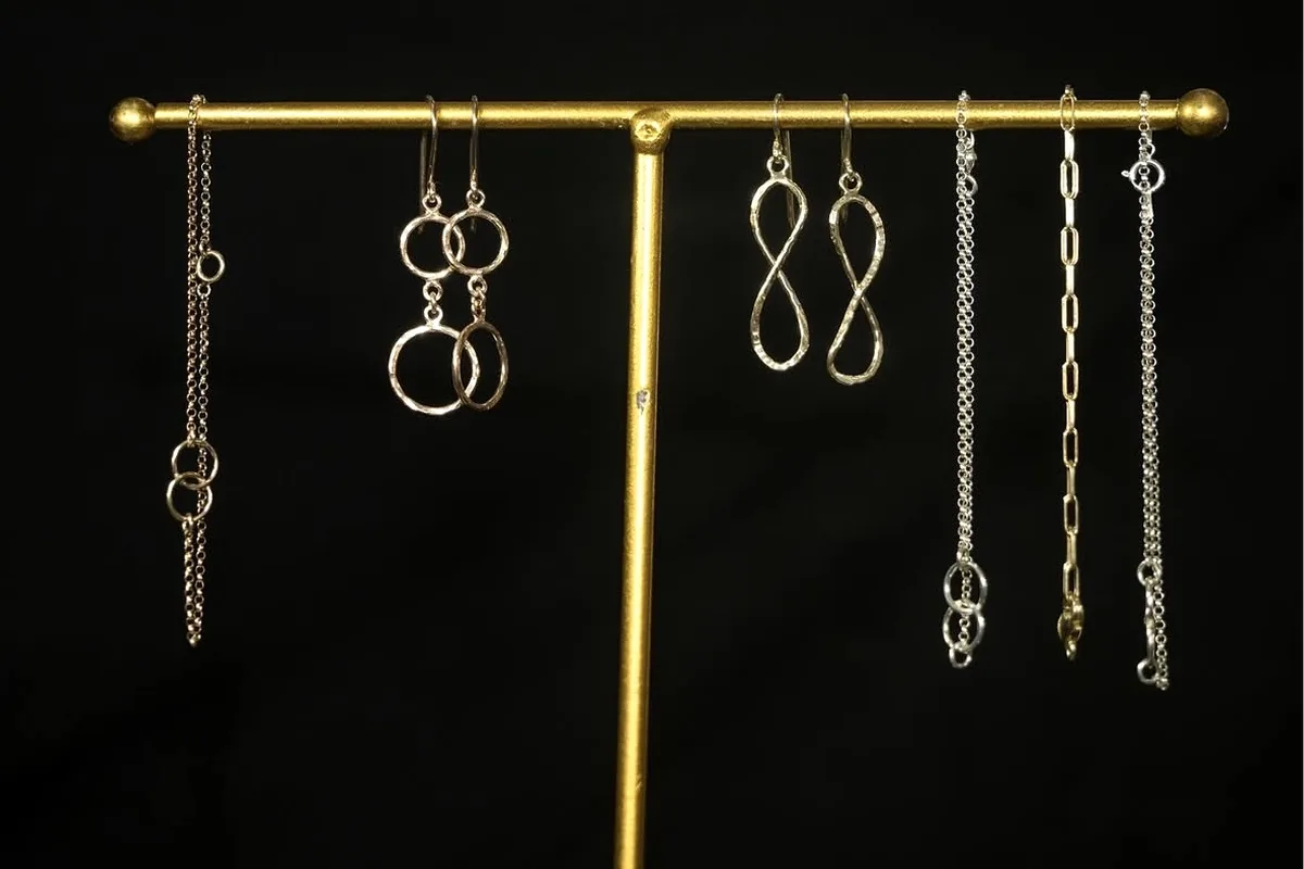 Mixed earrings and chains displayed on a brass jewellery stand against black.